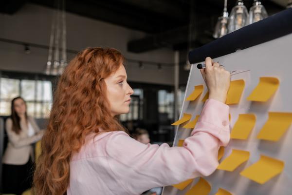 Woman with red hair writing on a whiteboard with sticky notes