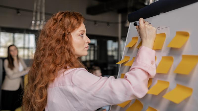 Woman with red hair writing on a whiteboard with sticky notes